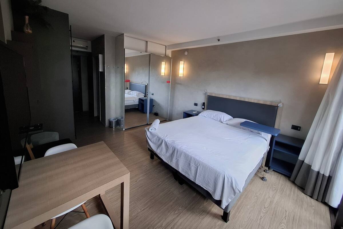 Une chambre d’hôtel comprenant un lit, des tables de chevet, un bureau, un miroir et une armoire.