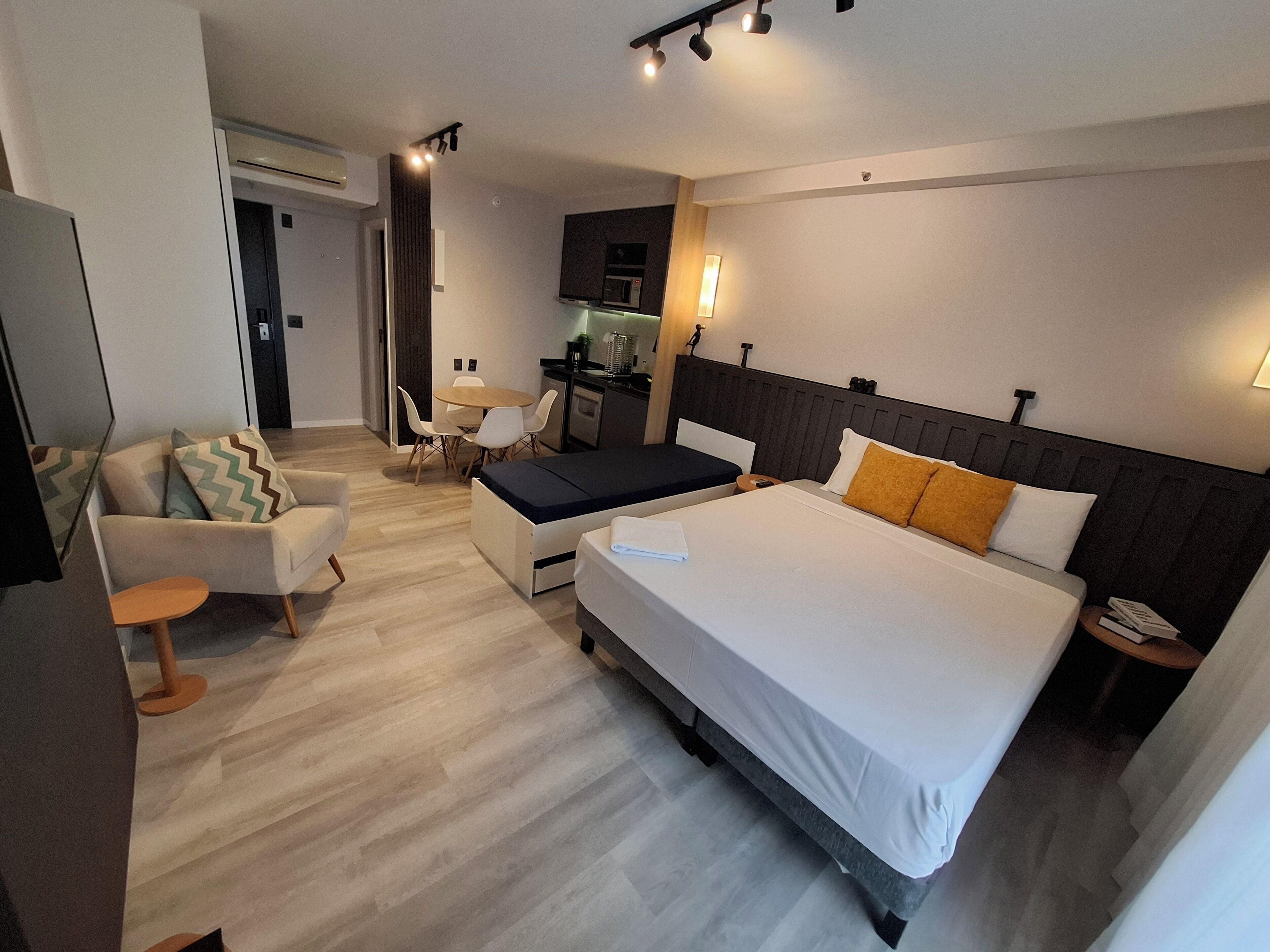 Una habitación de hotel moderna con una cama grande, un sofá, una mesa de comedor y una kitchenette.
