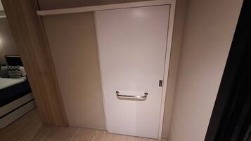 Una habitación con una puerta blanca cerrada, piso de madera y una cama con almohada a rayas.