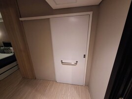Una habitación con una puerta blanca cerrada, piso de madera y una cama con almohada a rayas.