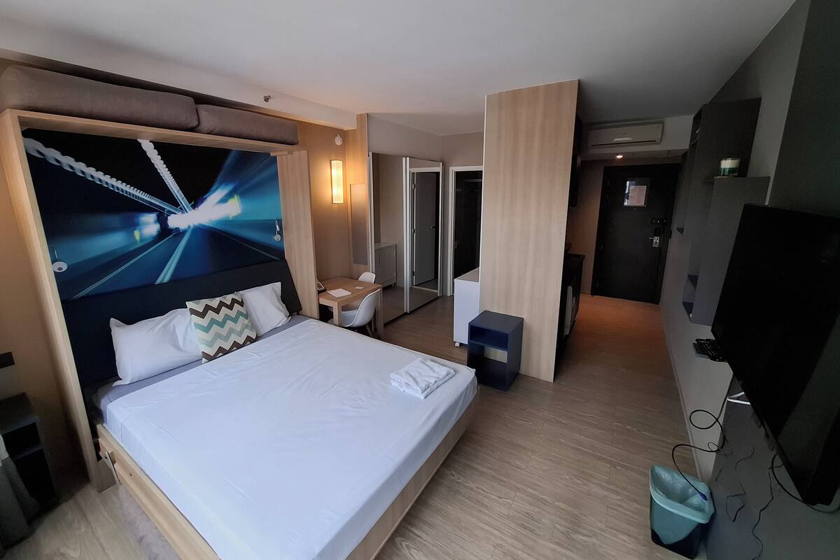 Une chambre d’hôtel avec un grand lit, un bureau, une chaise, une télévision et une salle de bain visible à travers une porte ouverte.