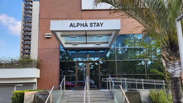L’entrée d’Alpha Stay se distingue par sa façade moderne en verre, un escalier doté de rampes en métal et une façade en briques.