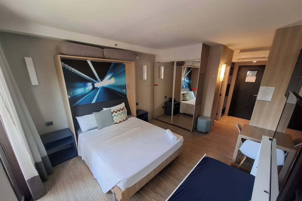Une chambre d’hôtel équipée d’un lit, d’un bureau, d’un miroir et d’un mur au design original.