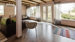 A spacious room with a wooden ceiling, a large window, a sofa, a chair, and a rug. - Ateljee by Interhome (Rääkkylä)