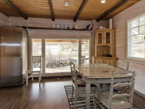 A kitchen with a stainless steel refrigerator, wooden cabinets, a dining table with chairs, and a view through the glass door. - Ateljee by Interhome (Rääkkylä)