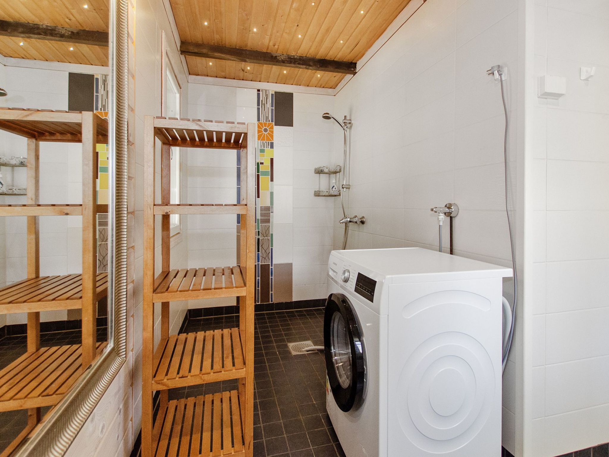 Une buanderie équipée d’un lave-linge, d’étagères en bois et d’une douche.