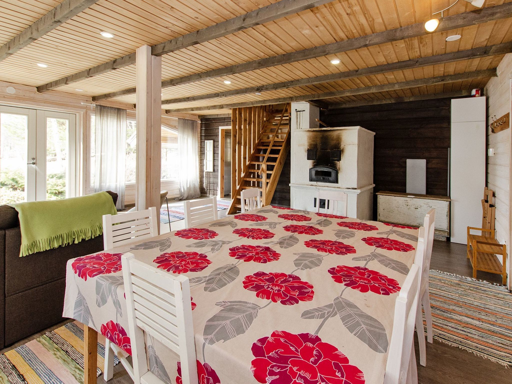 Et hyggeligt værelse med træloft, et spisebord med blomstret dug, en sofa og en trappe til et andet niveau.