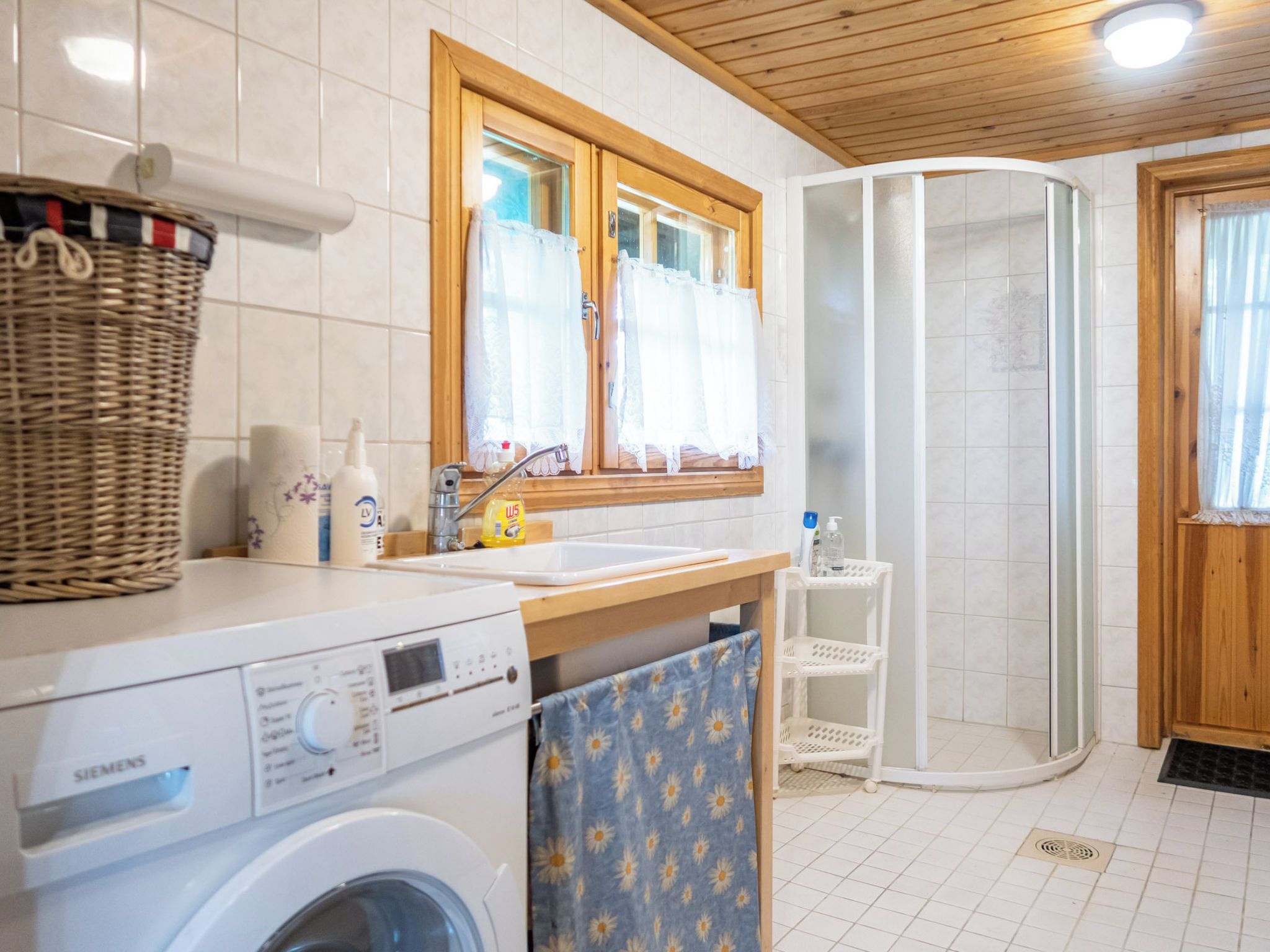 Moderni kylpyhuone, jossa on pesukone, pesuallas, suihku ja ikkuna, jossa on verhot.