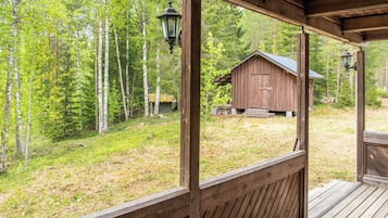 Puinen kuisti, josta avautuu näkymä maalaismaiseen mökkiin, jonka ympärillä kasvaa puita.