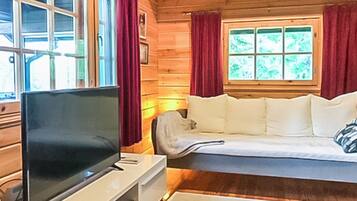 Ein Zimmer mit Fernseher auf einem Schrank, einem weißen Sofa und einem Fenster mit Vorhängen.
