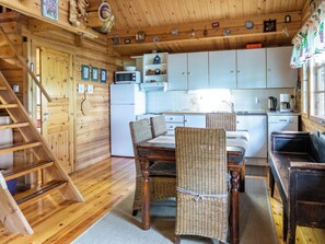 A wooden cabin interior with a dining area, kitchen, and a staircase.