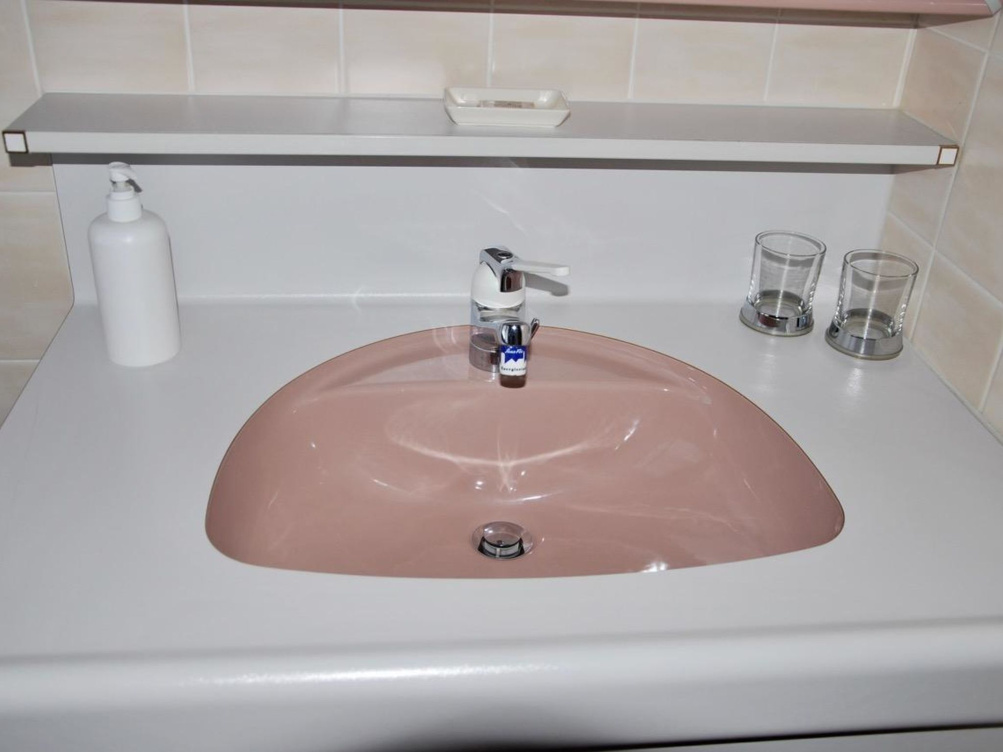 A bathroom sink with a pink basin, a soap dispenser, and two glasses on the countertop.