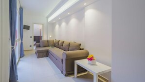 Una sala de estar moderna con un sofá modular beige, una mesa de centro blanca con un florero y un televisor de pantalla plana montado en la pared.