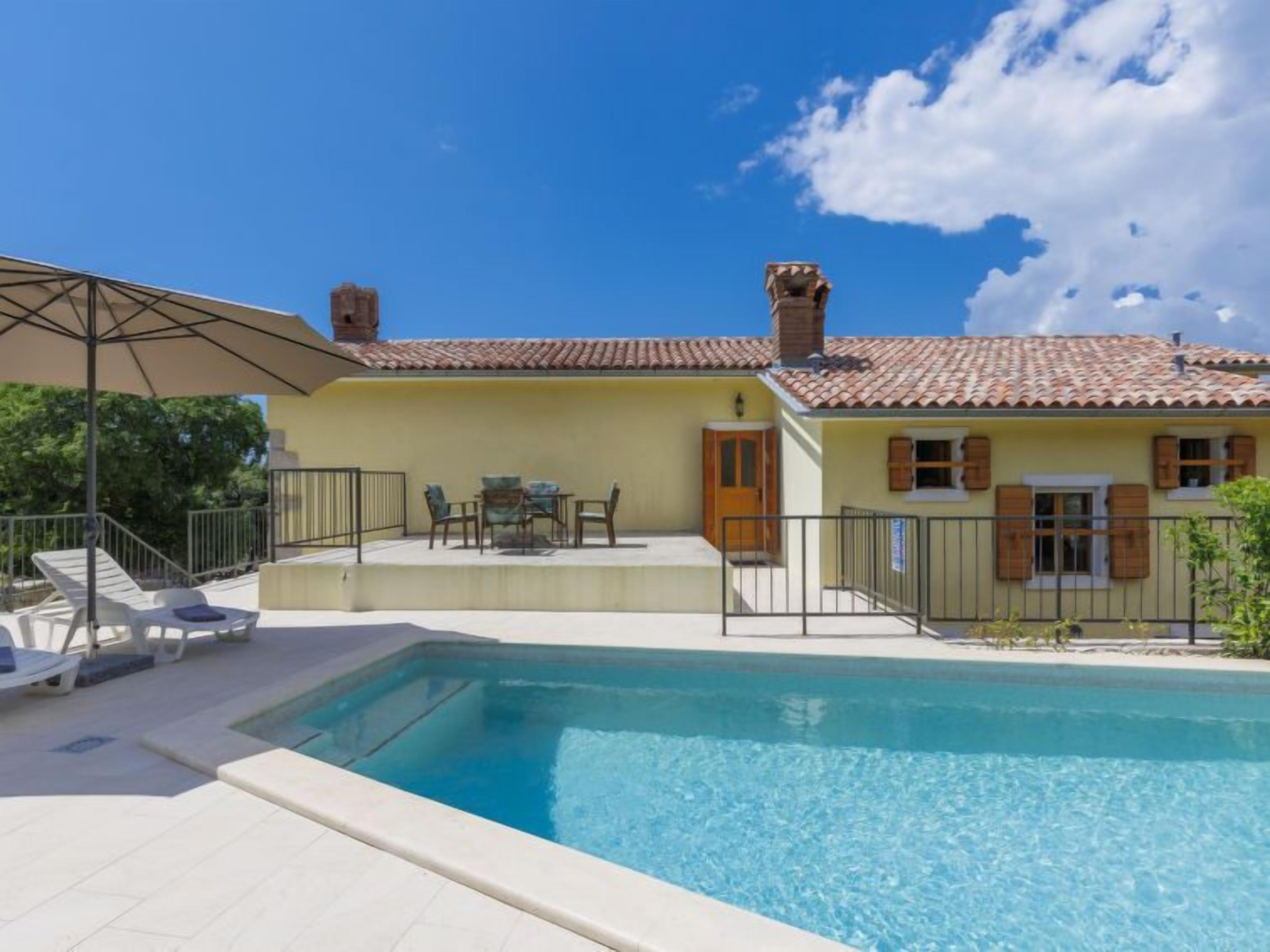 Zona junto a la piscina con piscina, mobiliario exterior y un edificio con tejado de baldosas.