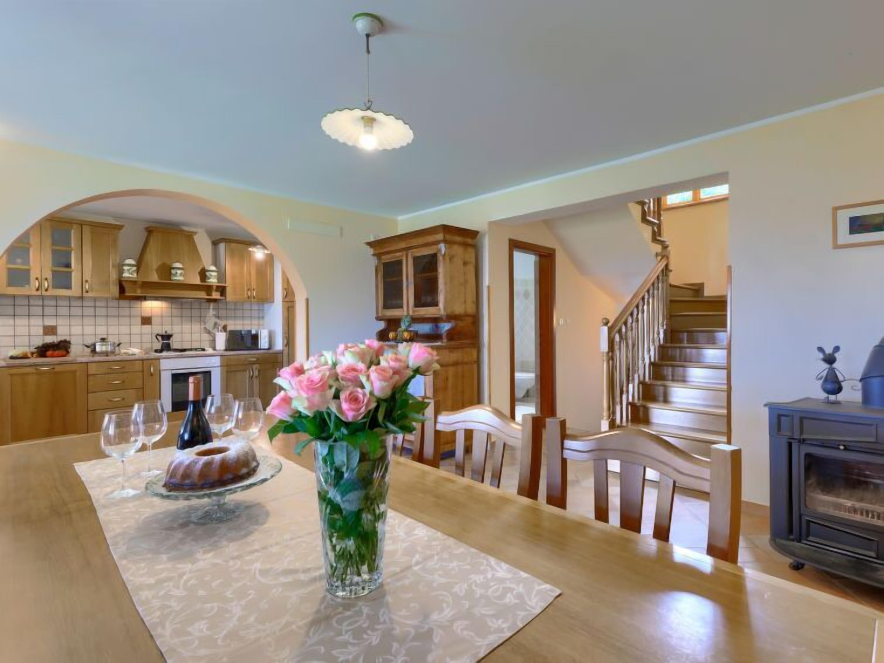 A kitchen with wooden cabinets, a dining table with a vase of flowers, and a staircase leading to another level.