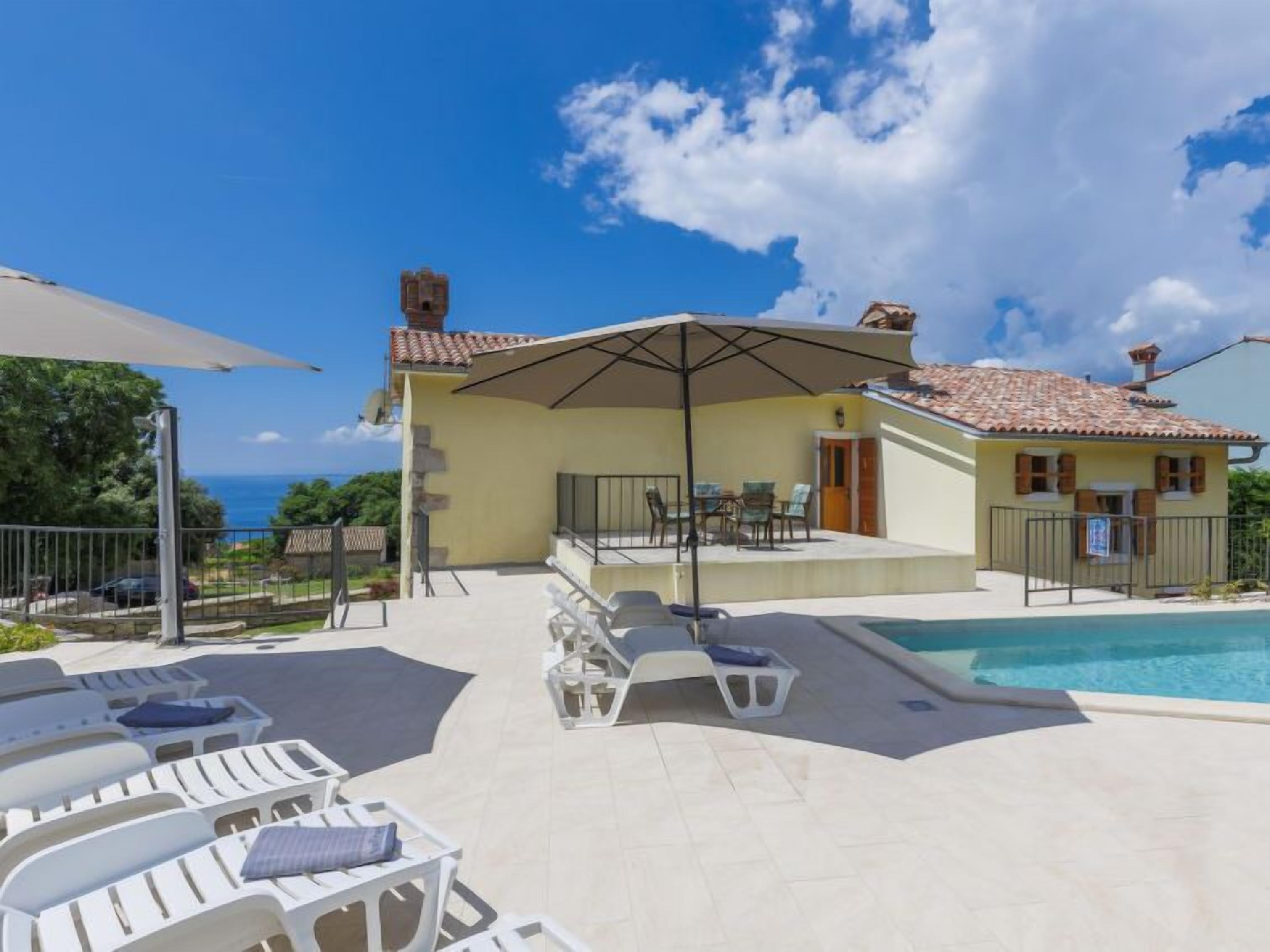 Un'area piscina con lettini, una zona salotto riparata e vista mare.