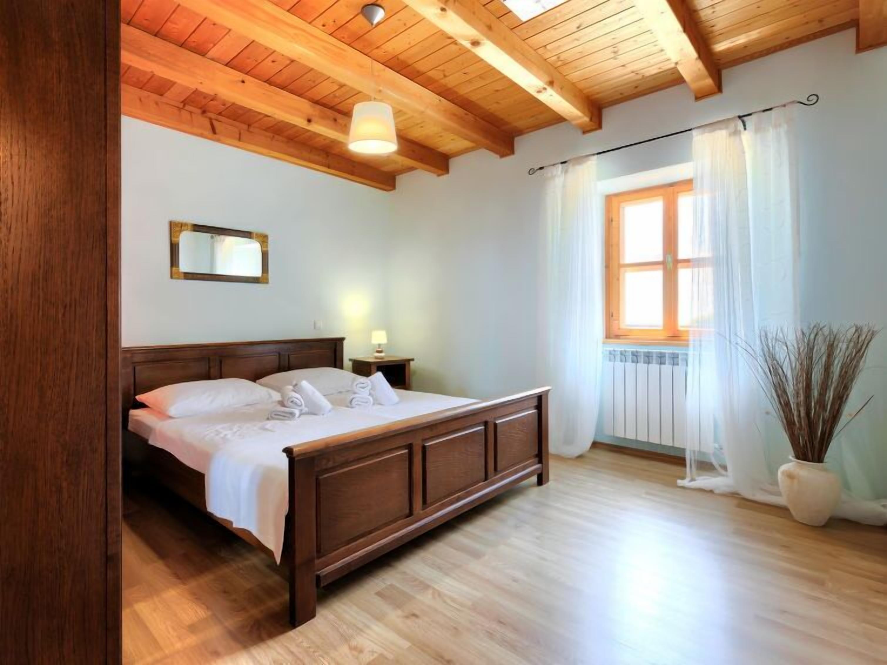 A bedroom with a wooden bed, a nightstand, a mirror, a window with curtains, and a radiator.
