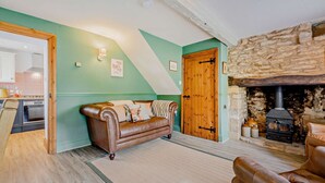 A cozy living room with a stone fireplace, a leather sofa, and a wooden door. - Characterful holiday cottage in the Cotswolds - Wren Cottage (Stow-on-the-Wold)