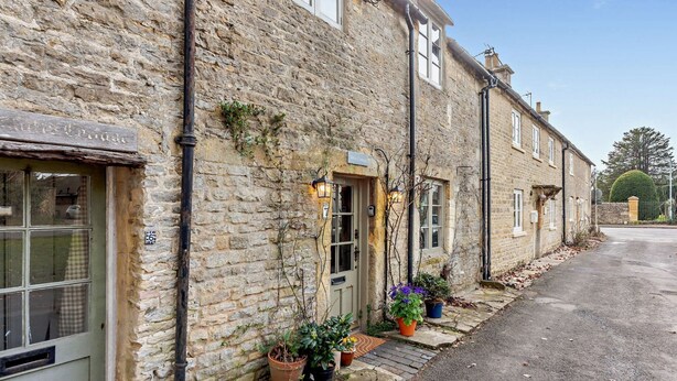 A stone building with a traditional facade, a door with a sign, and potted plants outside. - Characterful holiday cottage in the Cotswolds - Wren Cottage (Stow-on-the-Wold)
