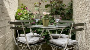 A small outdoor patio with a glass table and two folding chairs, surrounded by plants and a brick wall. - Characterful holiday cottage in the Cotswolds - Wren Cottage (Stow-on-the-Wold)