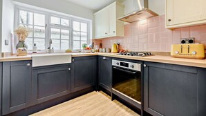 A modern kitchen with dark cabinetry, a stainless steel range hood, a yellow vintage toaster, and a window providing natural light. - Characterful holiday cottage in the Cotswolds - Wren Cottage (Stow-on-the-Wold)