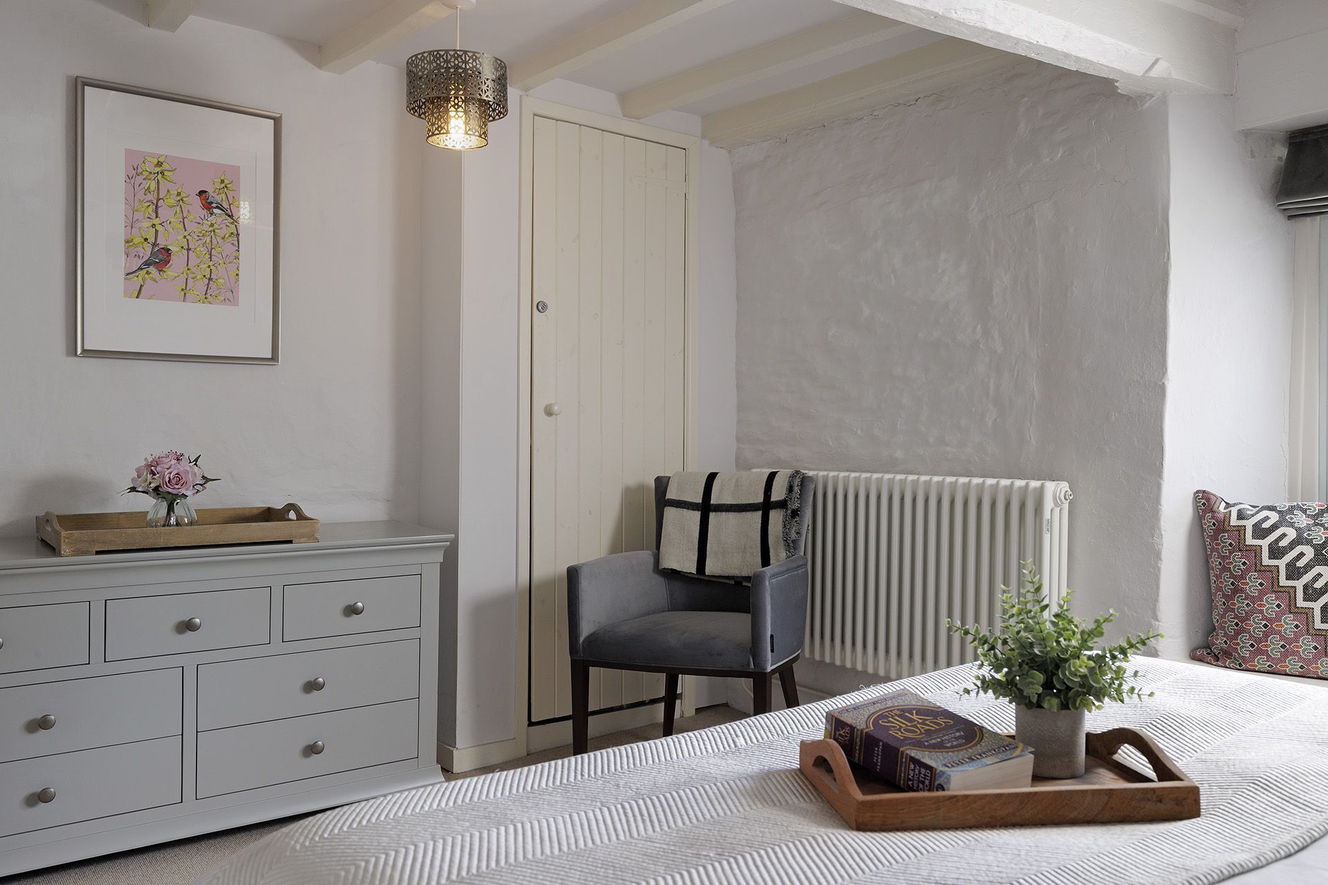 A bedroom with a bed, a dresser, a chair, a radiator, a plant, and a framed picture on the wall.