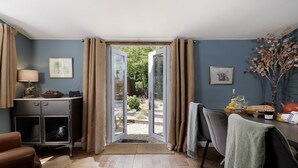 Quarto com piso de madeira, escrivaninha com abajur, cadeira, sofá e vista para área externa por uma porta de vidro.