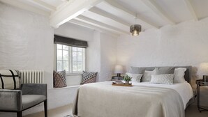 Quarto com cama grande, uma cadeira, janela e radiador.