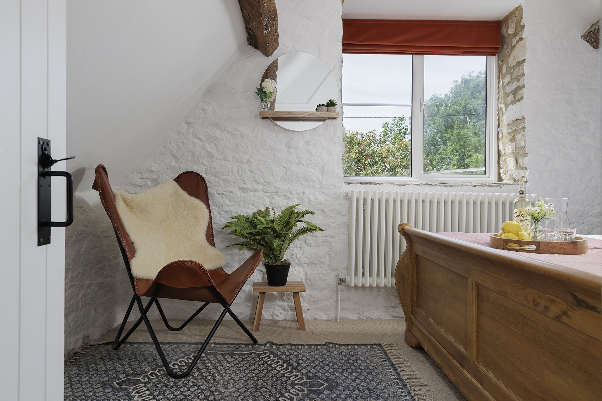 Ein gemütliches Zimmer mit Holzstuhl, einem kleinen Tisch mit Pflanze, einer Heizung und einem Fenster mit Blick auf Grünflächen.