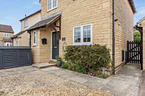 A two-story house with a stone facade, a front door, and a small garden area with gravel and plants. - Welcoming holiday home in Bourton on the Water - Ross House (Bourton-on-the-Water)