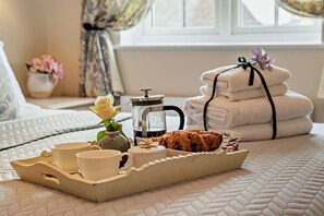 A breakfast tray with cups, a coffee pot, a croissant, and a rose on a bed with a quilted cover. - Welcoming holiday home in Bourton on the Water - Ross House (Bourton-on-the-Water)