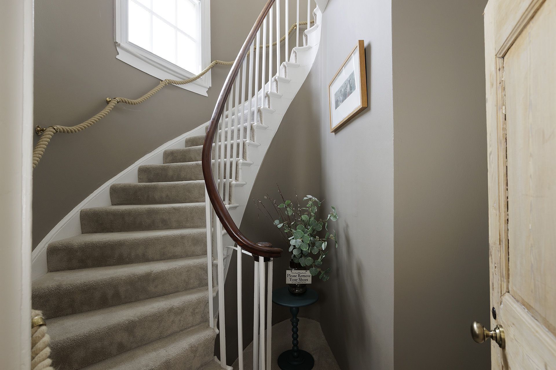 A carpeted staircase with white railings and a wooden handrail, leading to a door with a sign that reads "Please Remove Your Shoes."
