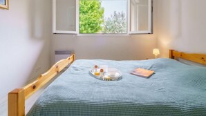 A small bedroom with a single bed, a window with an open shutter, a bedside table with a lamp, and a radiator. - Apartment Arnaïa by Interhome (Anglet)