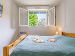 A small bedroom with a single bed, a window with an open shutter, a bedside table with a lamp, and a radiator.