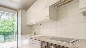 A modern kitchen with white cabinets, a stainless steel range hood, a double oven, and a large window with a view of greenery. - Apartment Arnaïa by Interhome (Anglet)