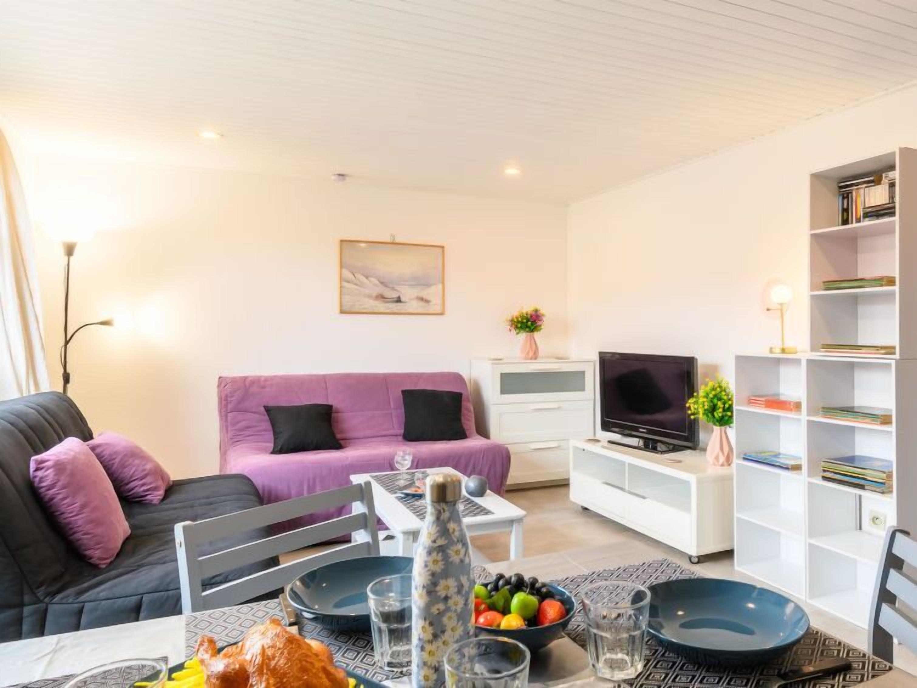 A modern living room with a sofa, TV, bookshelf, and dining area with plates and glasses.