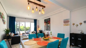 Un espace repas avec une table en bois, des chaises turquoise et un lustre moderne.
