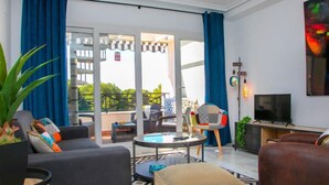 Un salon moderne avec un canapé, une table basse, un téléviseur et un balcon agrémenté de rideaux bleus.