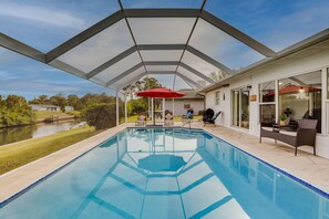 Piscina con un patio techado, mobiliario exterior y vista a un lago.