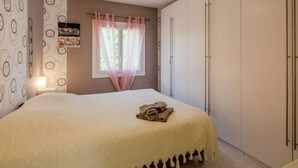A bedroom with a bed, a wardrobe, a window with curtains, and a wall-mounted shelf.