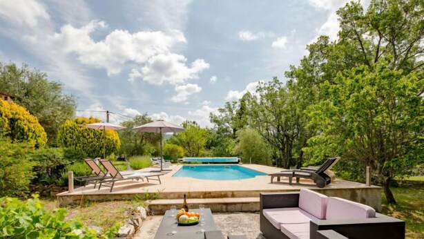 A pool area with lounge chairs and a table with fruit and a bottle.