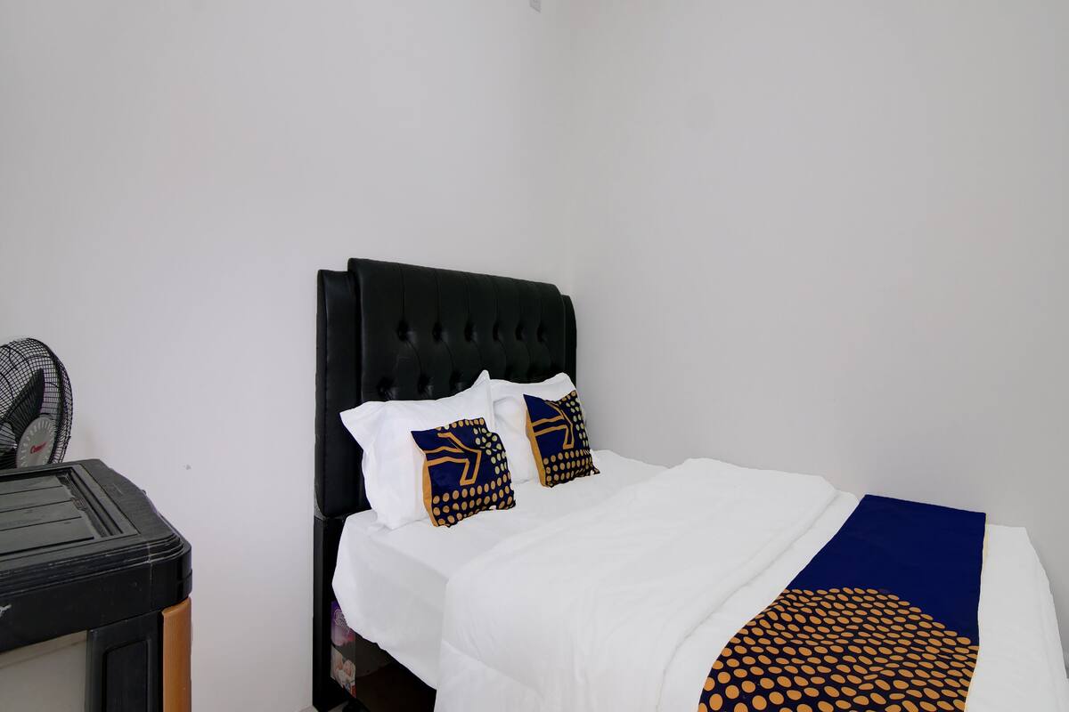 Een net opgemaakt bed met een zwart hoofdbord, wit beddengoed en twee decoratieve kussens met een geometrisch patroon.