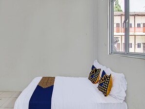 Un lit bien fait, avec une literie blanche et deux coussins décoratifs à motifs géométriques.