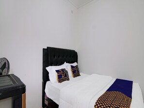 Un lit bien fait, avec une tête de lit noire, une literie blanche et deux coussins décoratifs à motifs géométriques.