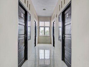Un couloir doté d’un sol carrelé, de portes noires et d’une fenêtre avec des stores horizontaux.