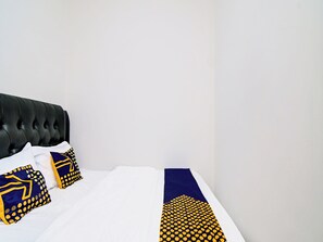 Un lit bien fait, avec des draps blancs et un couvre-lit à motifs bleus et jaunes.