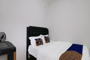 Una cama con cabecera negra, ropa de cama blanca y dos almohadones con un diseño azul y dorado.