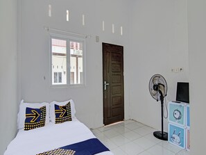 Une chambre à coucher avec un lit, une fenêtre, une porte et un ventilateur sur pied.