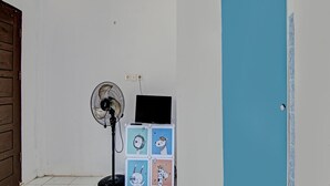 Ein Zimmer mit einer weißen Tür, einer blauen Tür, einem Ventilator und einem kleinen Tisch mit einem Laptop.