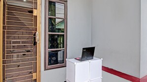 Ein Zimmer mit Holztür, einem Fenster mit zerbrochenen Scheiben und einem weißen Schrank mit einem Laptop darauf.